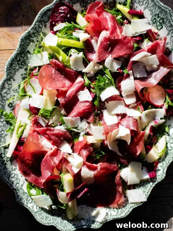 A salad with Bresaola, radicchio, radish and apple in direct sunlight on a large green and white platter.