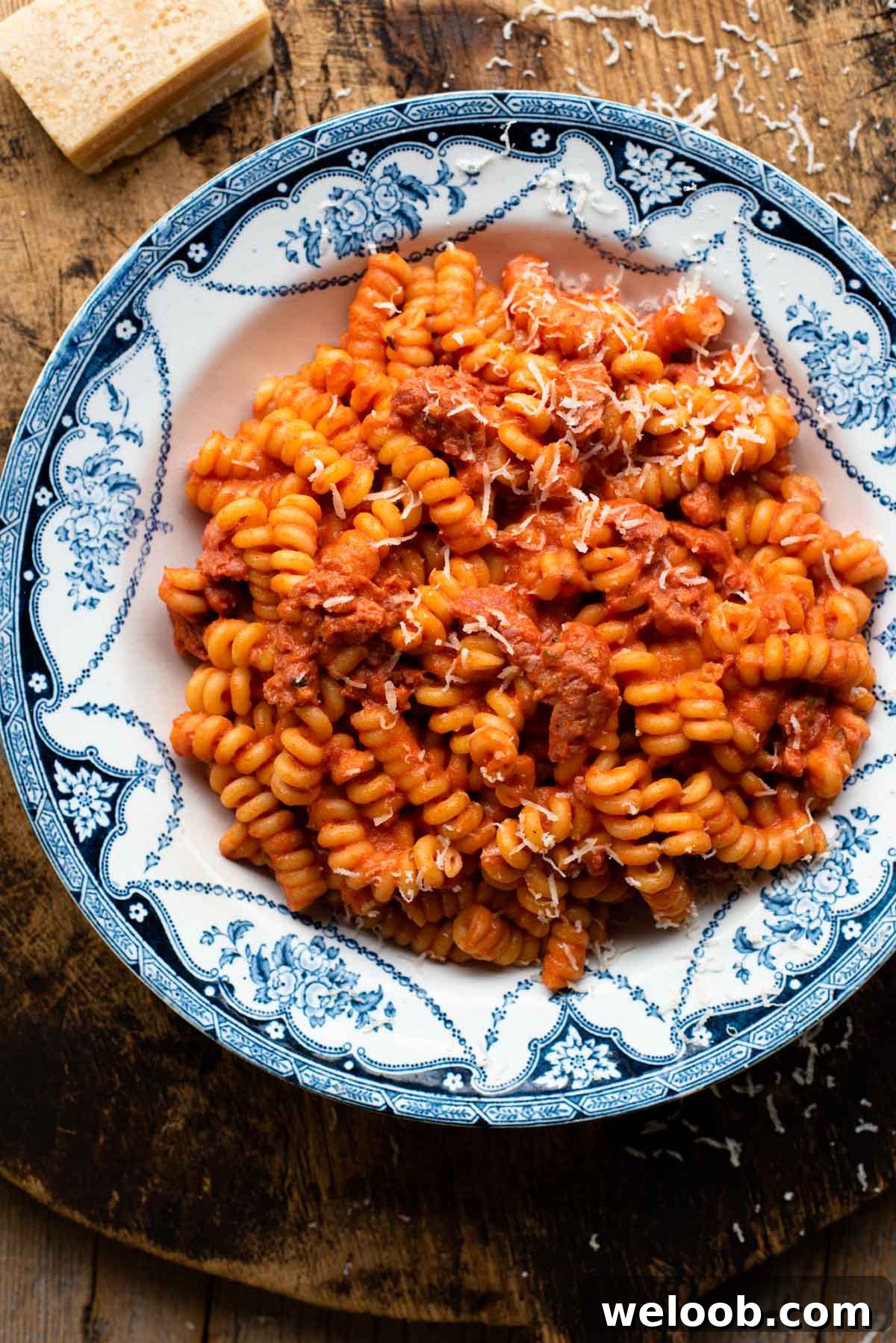 Creamy tomato pasta with sausage in a blue patterned bowl on a wooden serving board. 