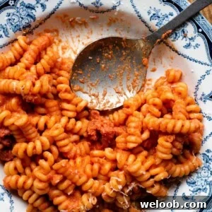 A close up cropped image of creamy tomato sausage pasta in a blue bowl with a serving spoon