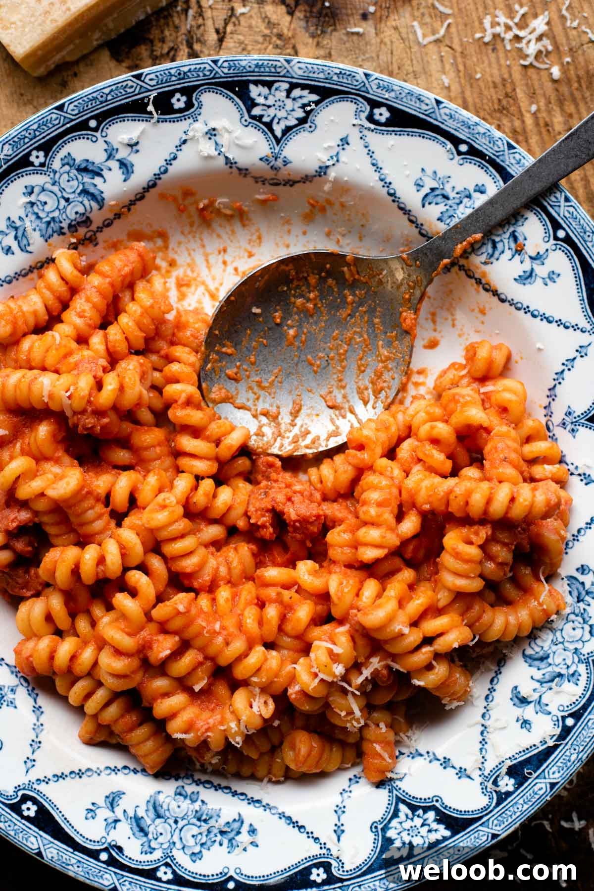 An overhead shot of creamy tomato pasta with Italian sausage in a blue patterned bowl with a serving spoon at the side.