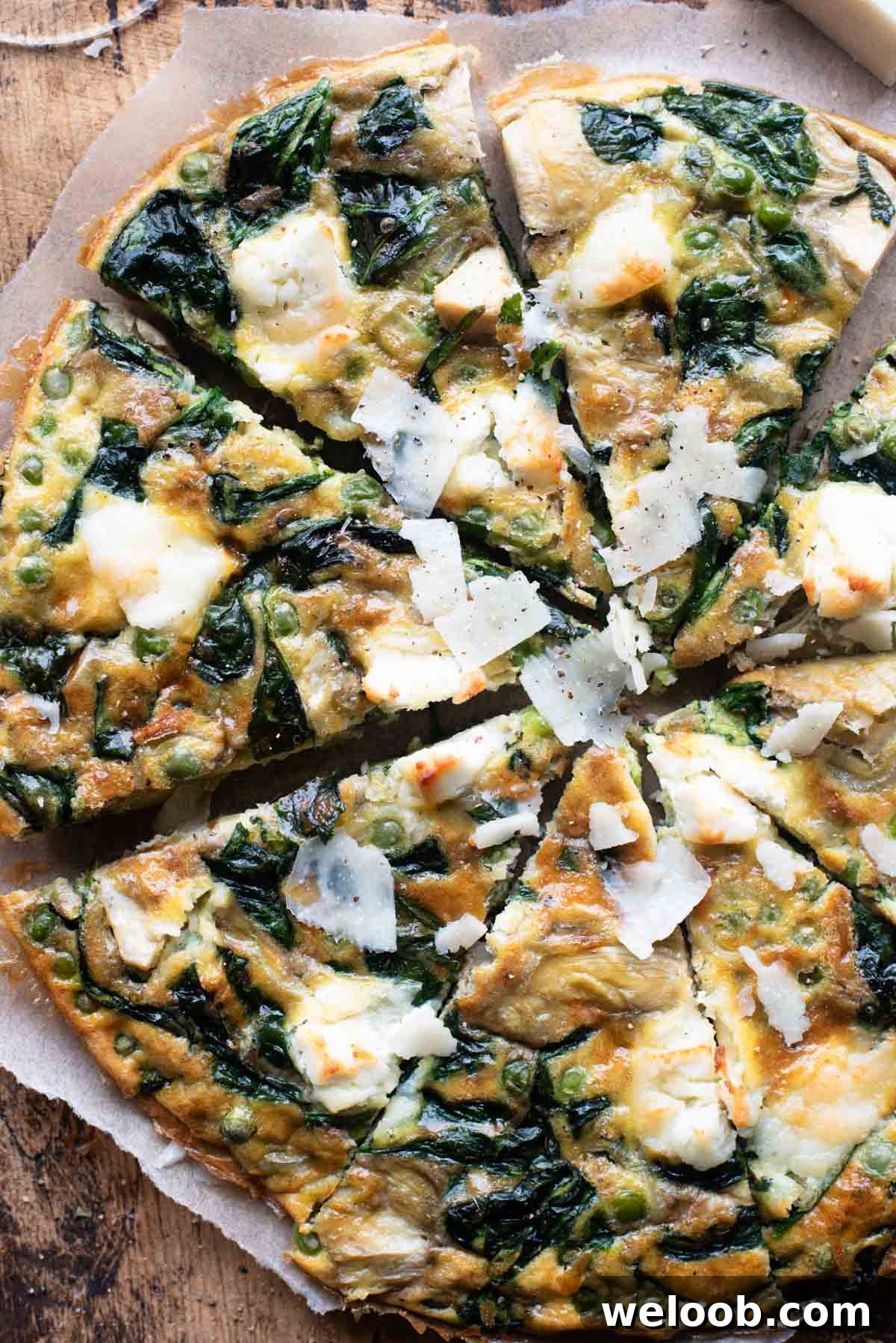 An overhead shot of a spinach and artichoke frittata cut into slices sitting on a wooden cutting board.