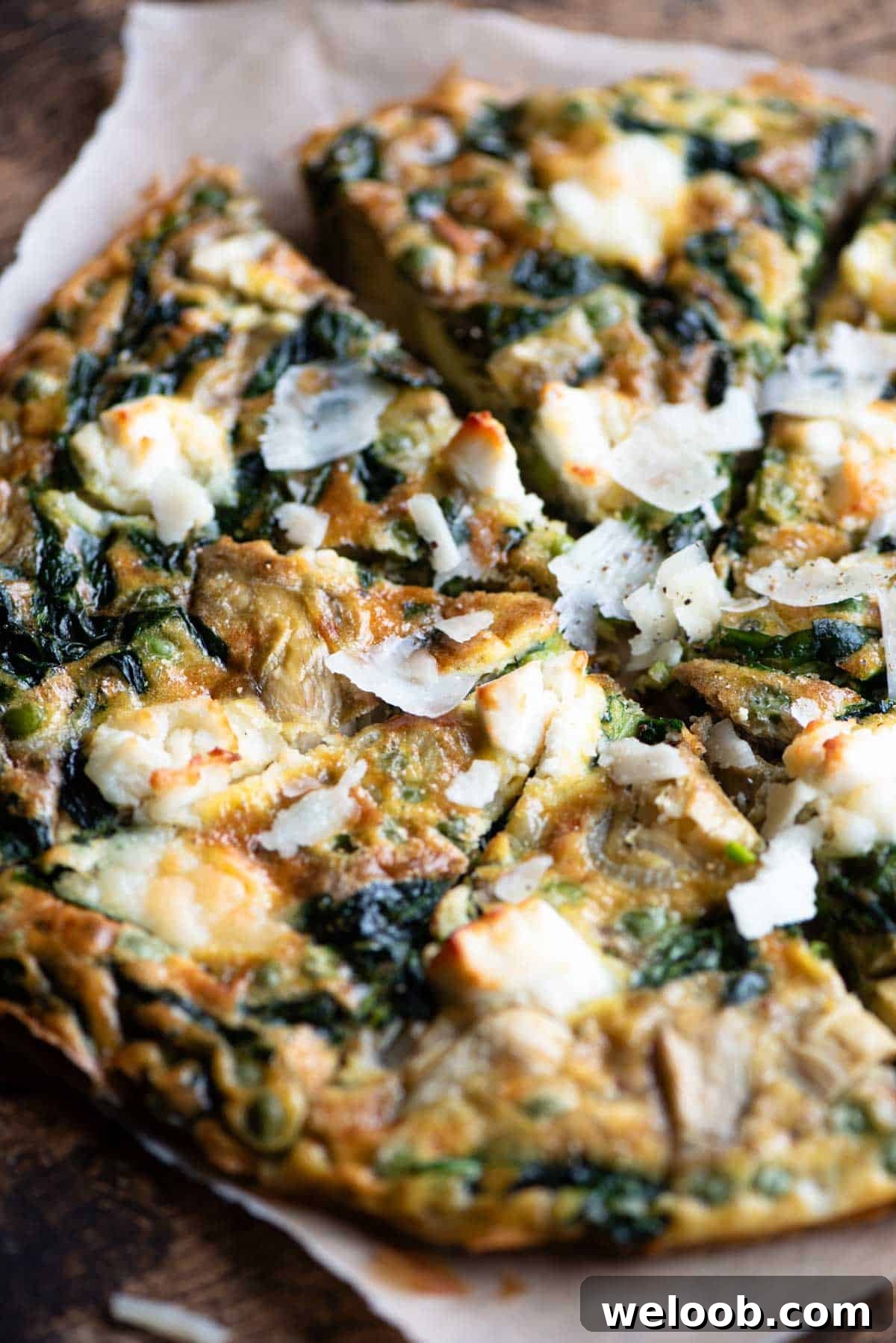 A close up of a spinach and artichoke frittata topped with goat's cheese cut into slices.