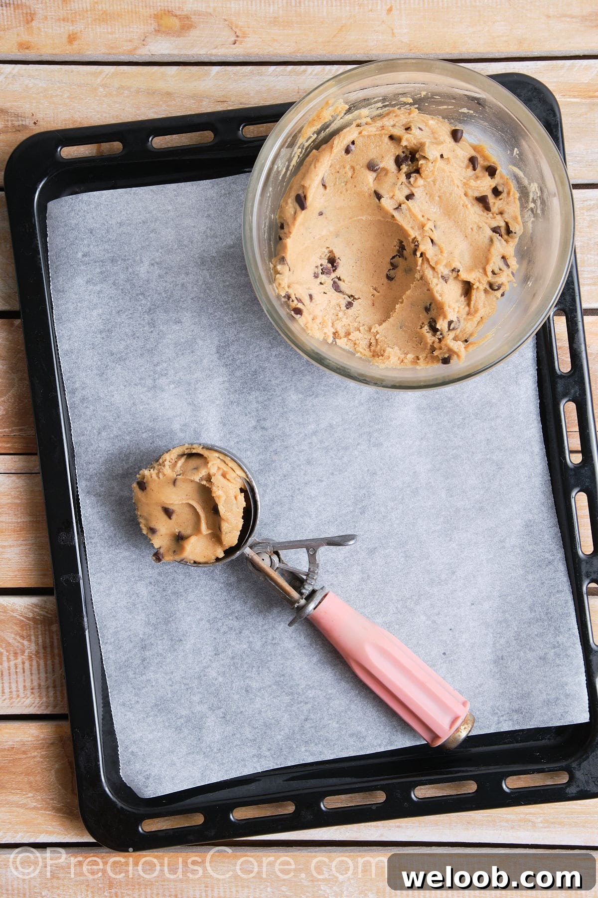 A scoop filled with the cookie dough, placed on a lined baking sheet