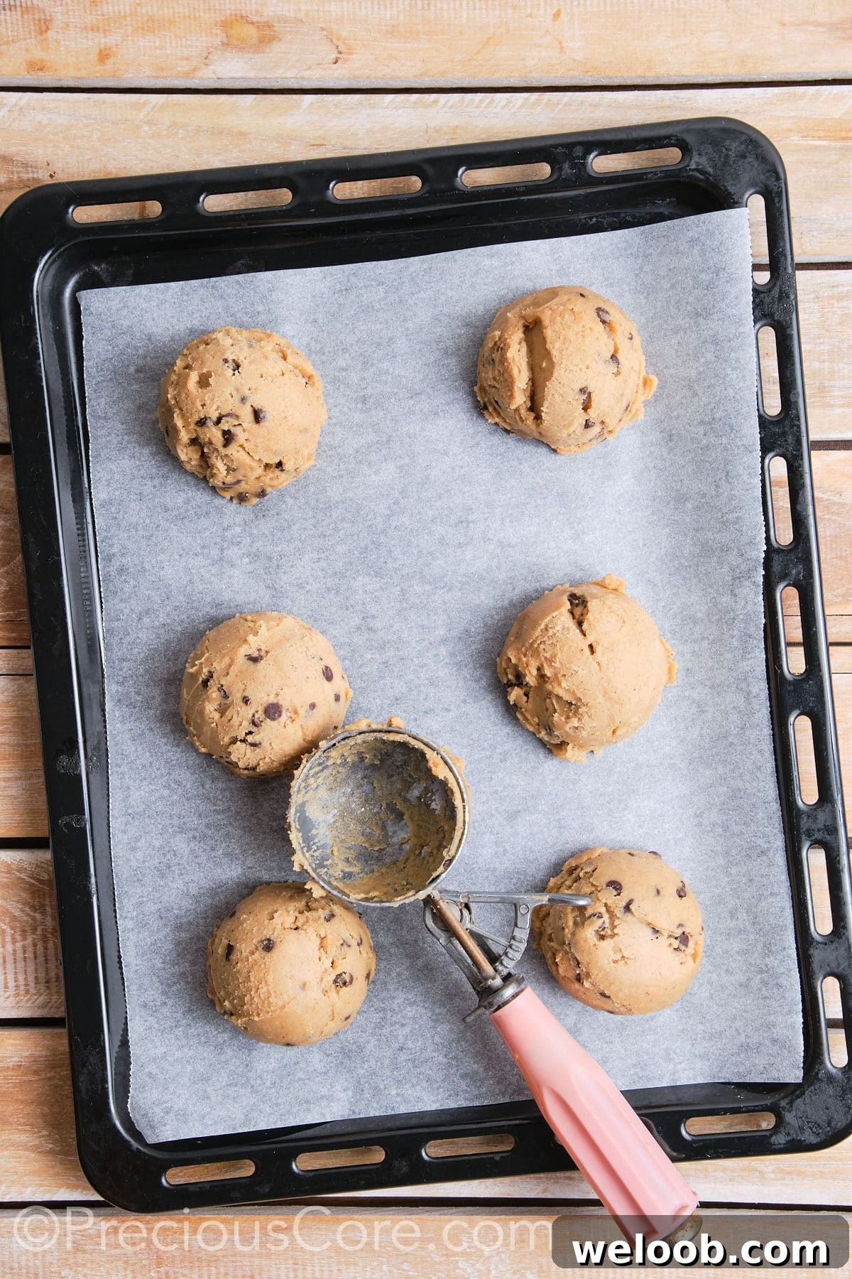 Baking sheet lined with parchment paper with 6 scoops of cookie dough