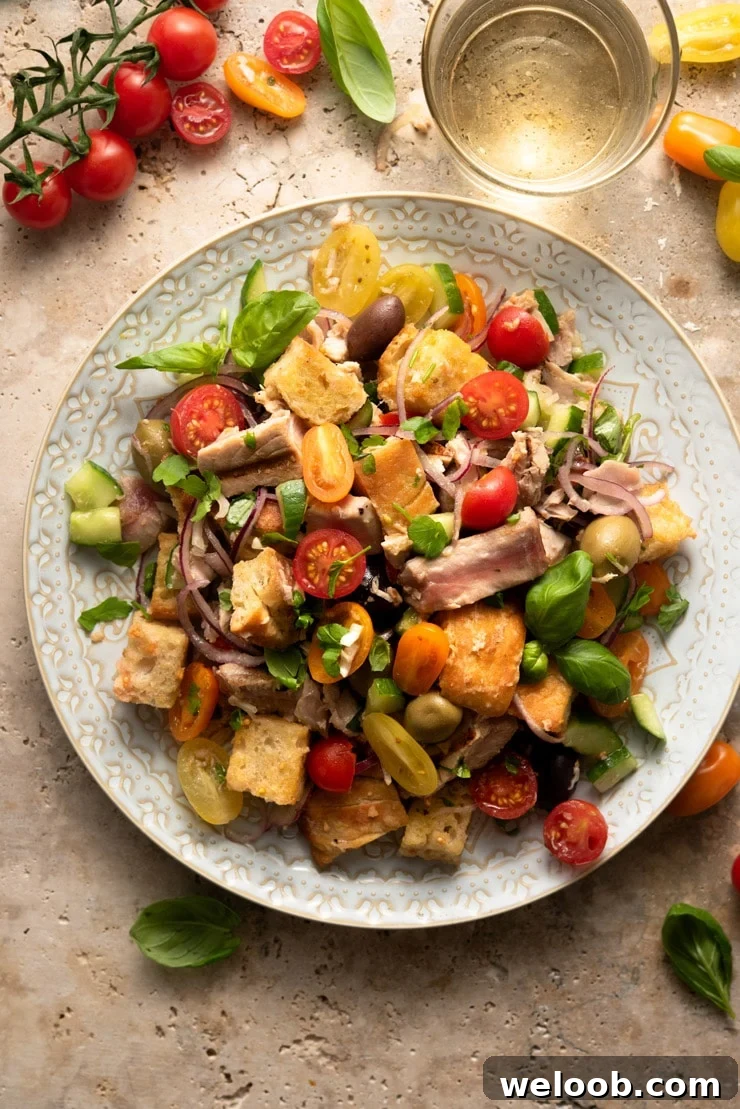 An overhead shot of a tuna panzanella salad on a large plate with tomatoes and basil scattered around
