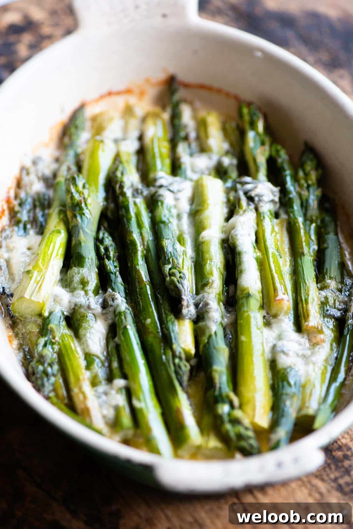 A side shot of roasted asparagus in an oval baking dish topped with gorgonzola.