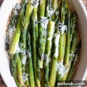 A cropped square image of roasted asparagus in a baking dish topped with gorgonzola.