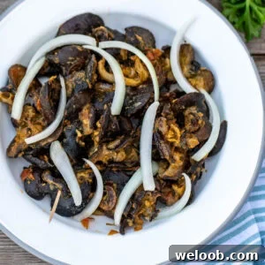 Cameroonian snails on a white plate topped with sliced onions.