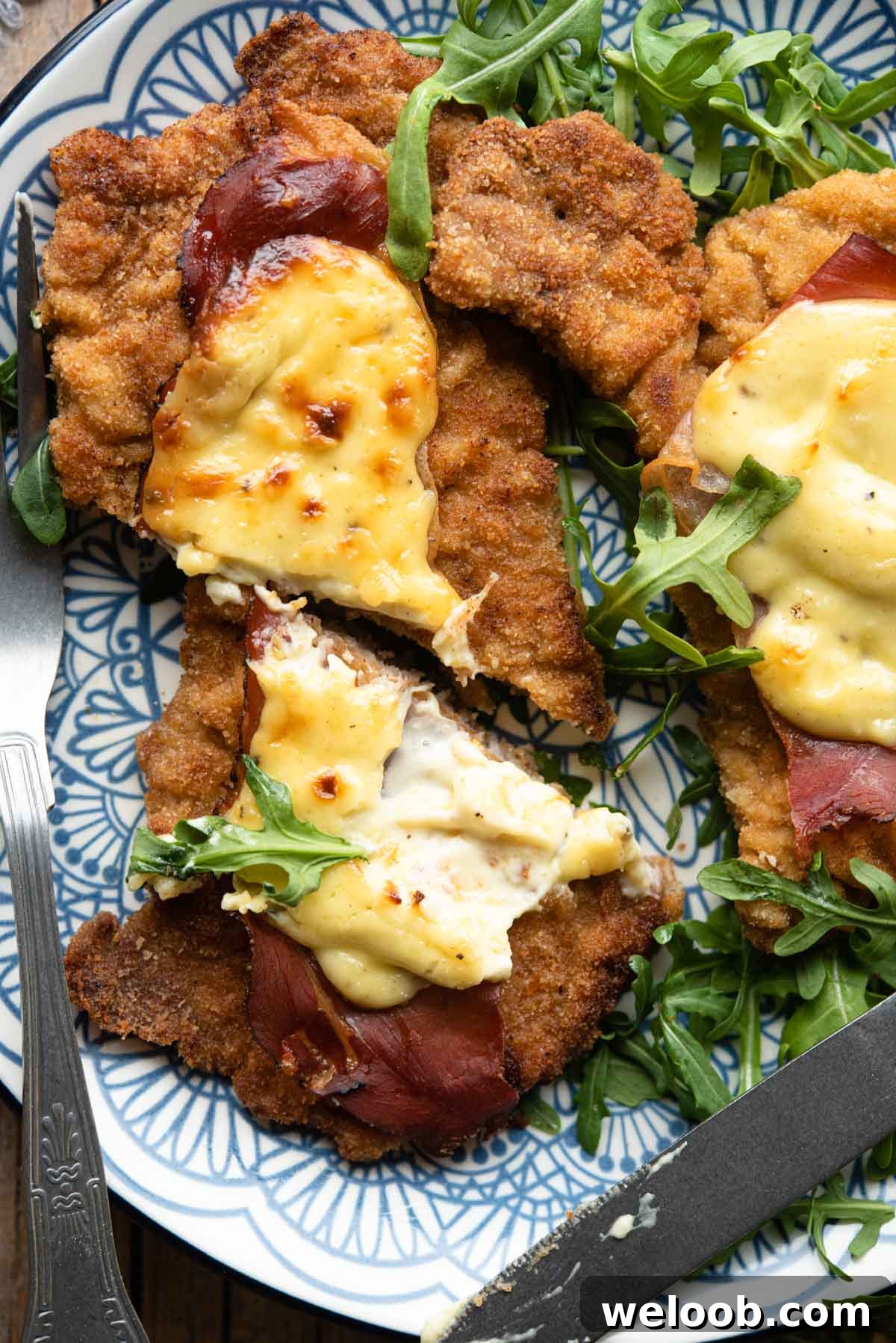 A close up of a veal cutlet cut in half with parmesan cream and prosciutto on top