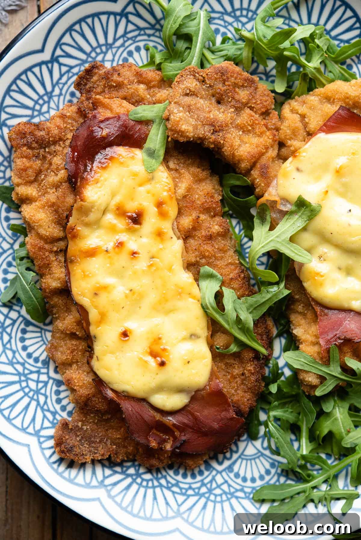 An overhead shot of breaded veal cutlets on a plate topped with parmesan cream and prosciutto