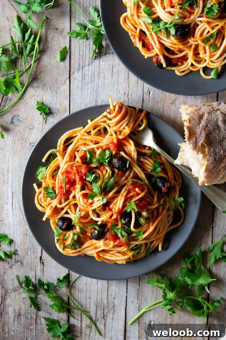 An overhead shot of a plate of spaghetti with puttanesca sauce and chopped parsley scattered around
