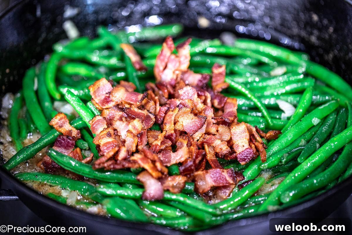 Crispy bacon over green beans in skillet.