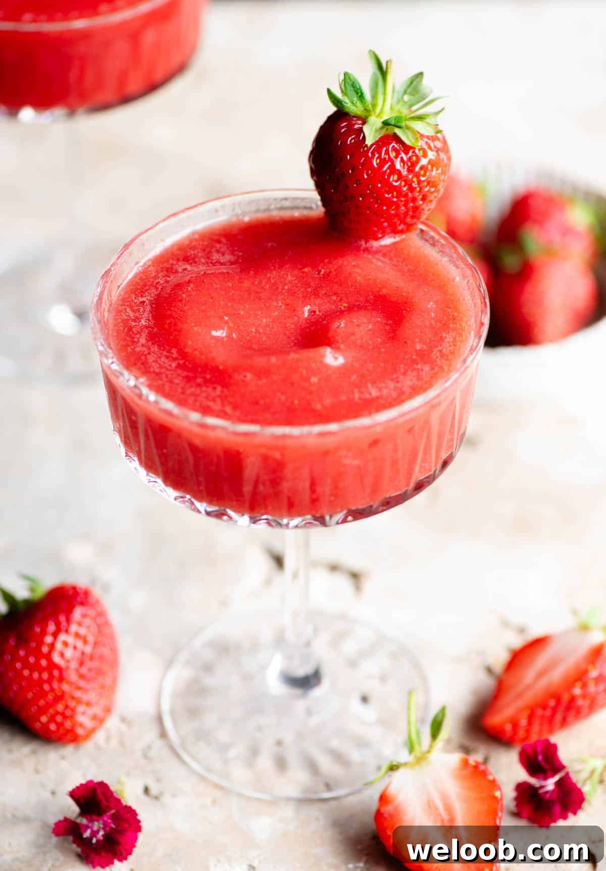 A close up of a frozen strawberry cocktail in a cocktail glass garnished with a strawberry.