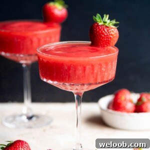 A close up of a frozen strawberry cocktail in a glass garnished with a whole strawberry.