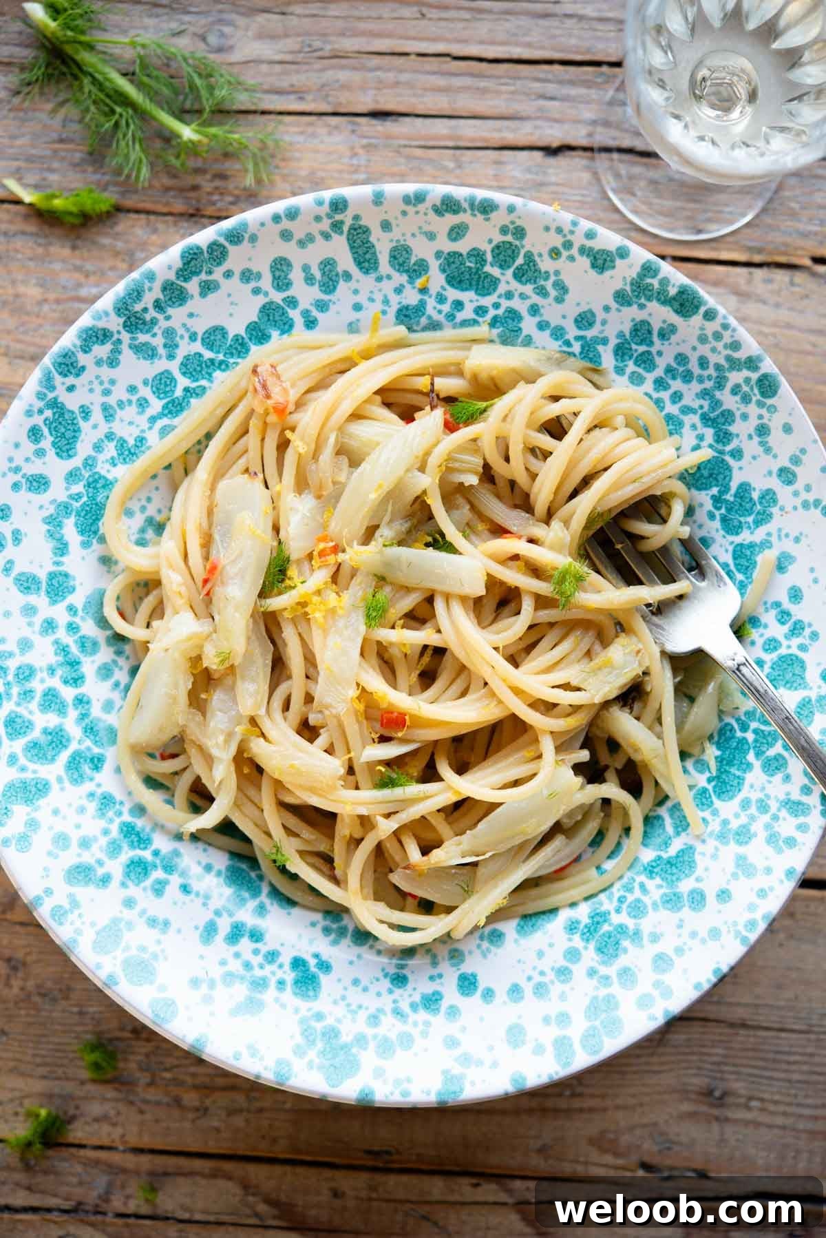 An overhead shot of roasted fennel pasta in a blue spotted bowl sitting on a rustic wooden surface.