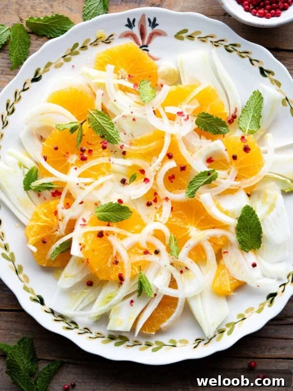 An overhead shot of a fennel and orange salad on a plate topped with mint leaves and pink peppercorns.