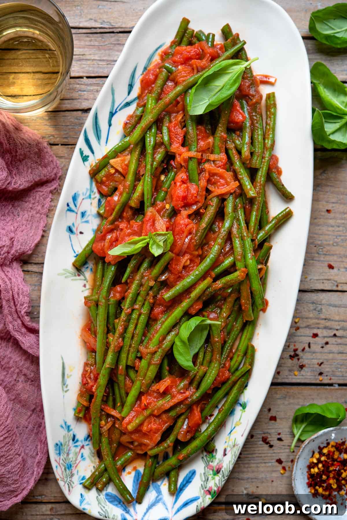 An overhead shot of Italian green beans tossed in a tomato sauce on an oval plate