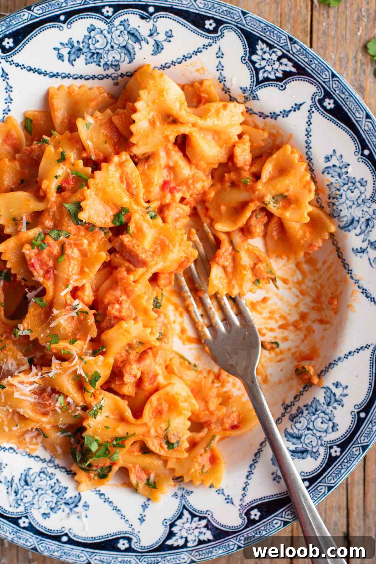 A close up of farfalle pasta in a blue and white floral bowl with a fork.