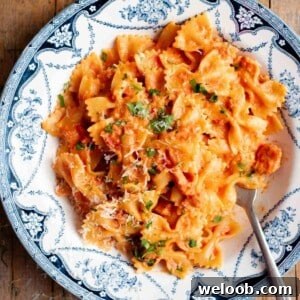 A close up of farfalle pasta in a garlic and chilli sauce with a fork at the side. The bowl is vintage style in blue and white.