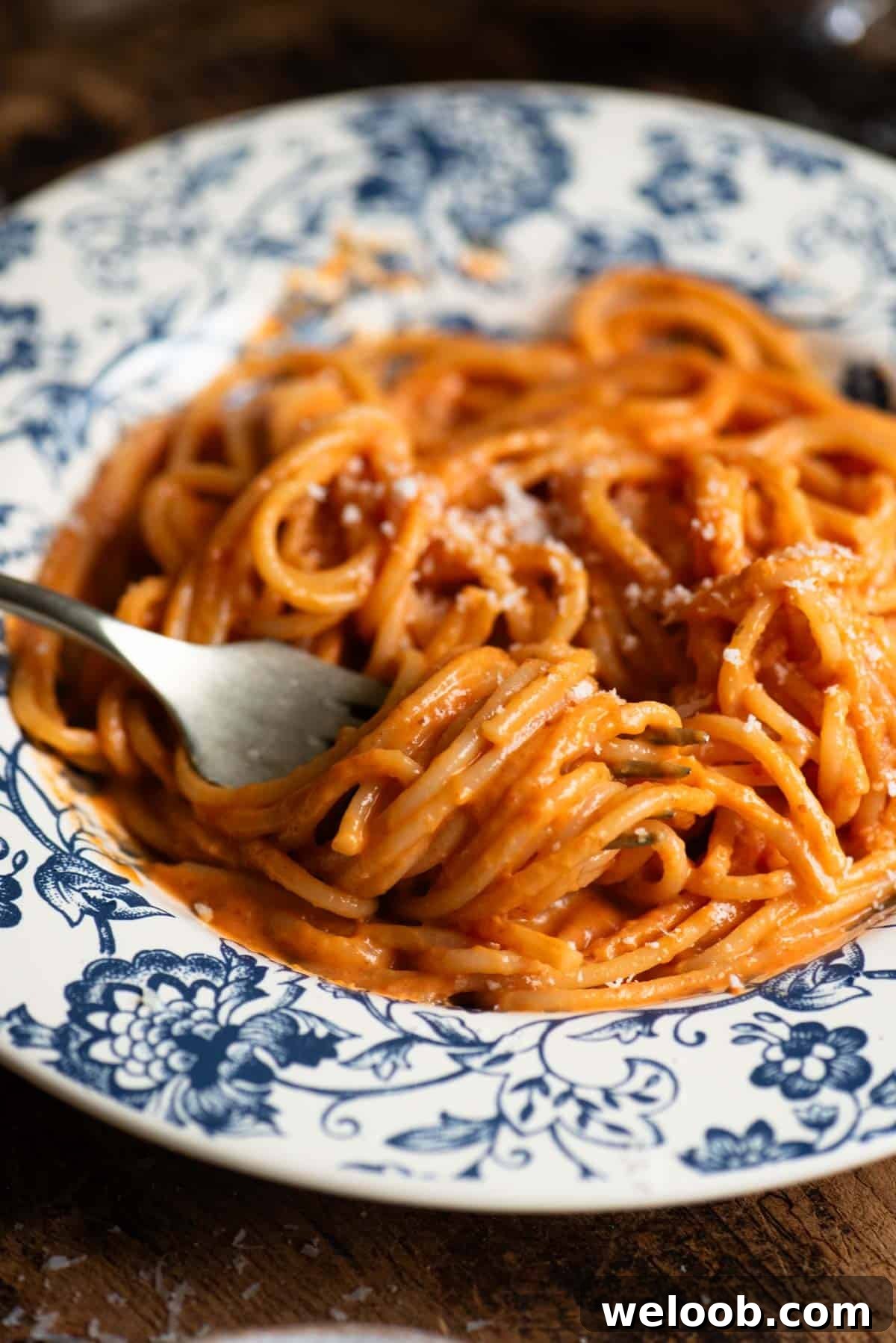 A close up of spaghetti with creamy roasted red pepper sauce rolled around a fork.
