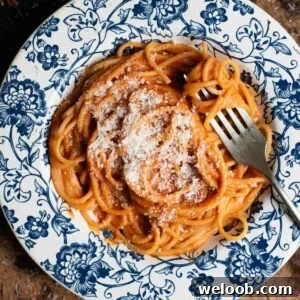 A close up of creamy roasted red pasta in a blue floral bowl sitting on a wooden board.