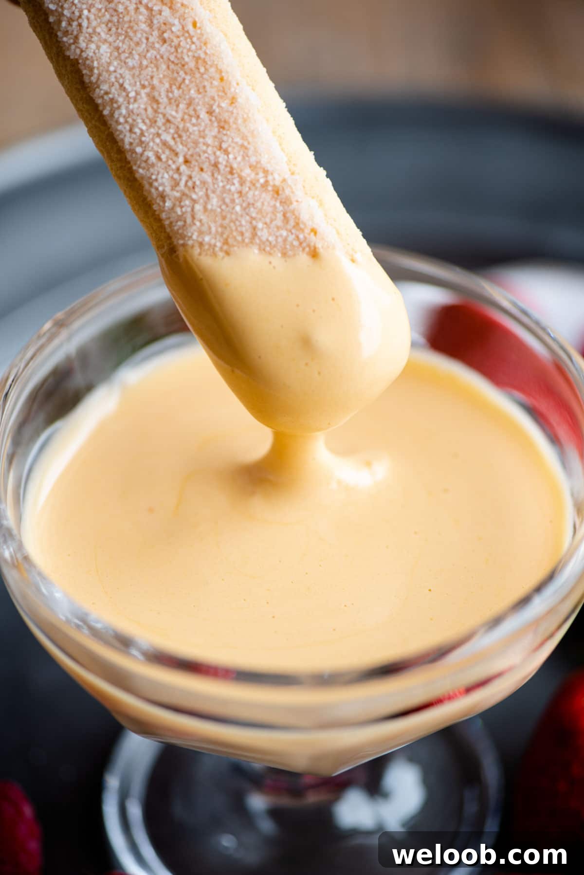 A close up of a savoiardi cookie being dunked into zabaglione