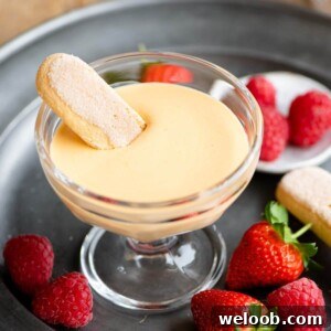 Zabaglione in a glass serving dish with a savoiardi biscuit dunked in and berries at the side