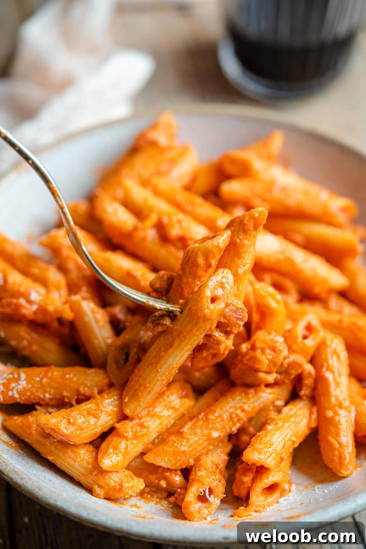 A close up of a fork picking up pasta with a tomato vodka sauce