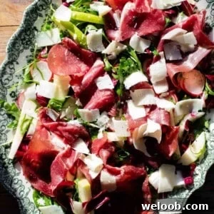 A close up of a bresaola salad topped with shavings of Parmigiano Reggiano on a servings plate.