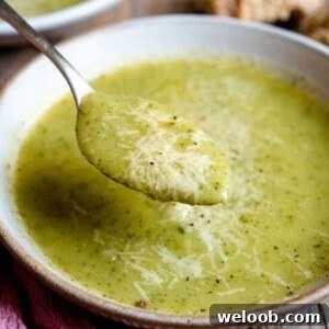 A close up of a spoonful of zucchini potato soup topped with parmesan.