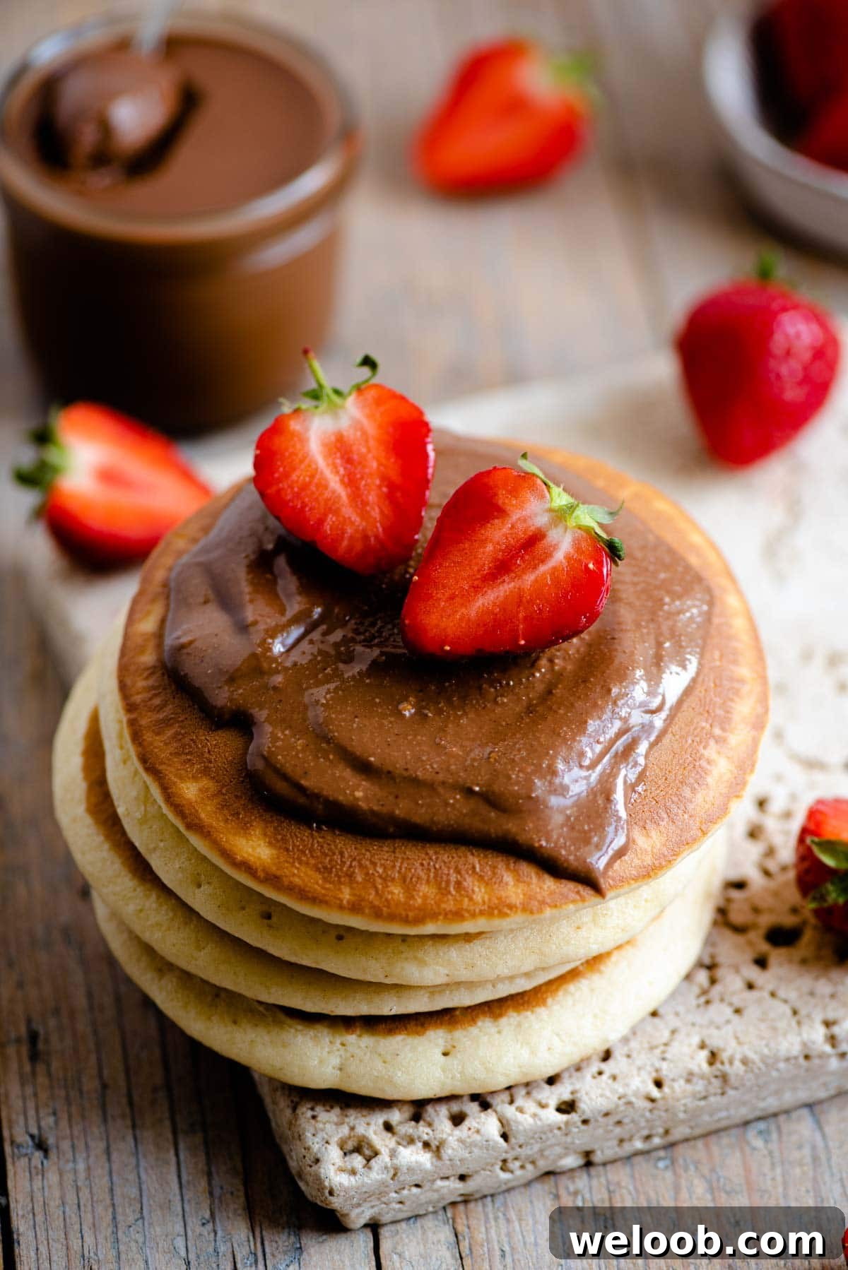 A close up of a stack of pancakes topped with Nutella and strawberries