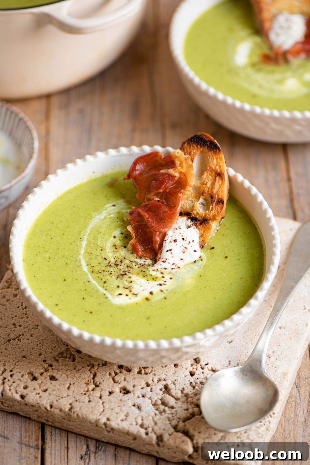 Green pea soup in a bowl topped with yogurt and crispy prosciutto