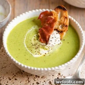 A close up of green pea soup with a slice of bread and prosciutto at the side