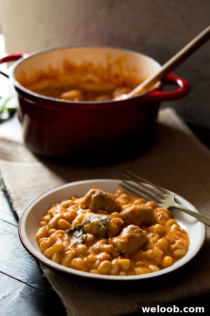 A close up of Tuscan bean stew with sausages on a plate with a fork, pot in the background.
