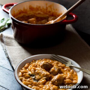 Tuscan bean stew with sausages on a plate, fork at the side and pot in the background