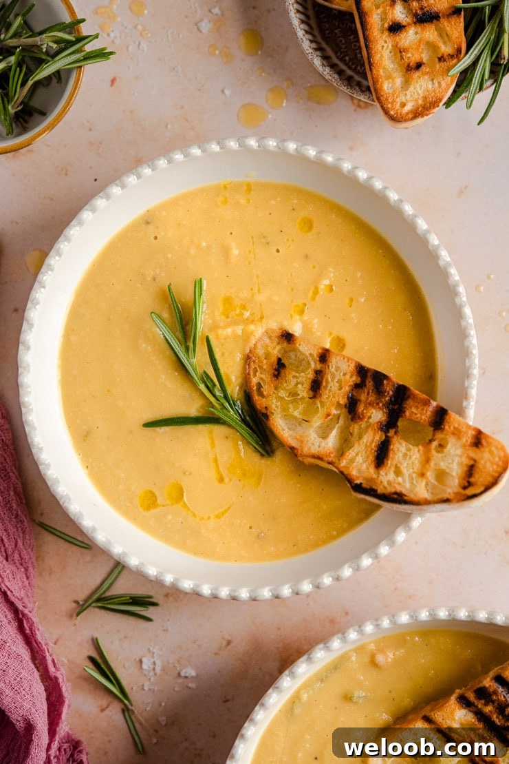An overhead shot of chickpea soup in a bowl topped with a sprig of rosemary