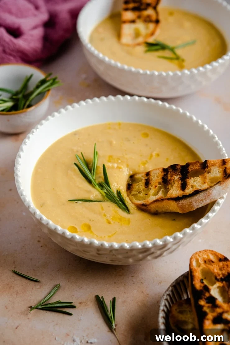 A side shot of chickpea soup in a bowl topped with crusty bread