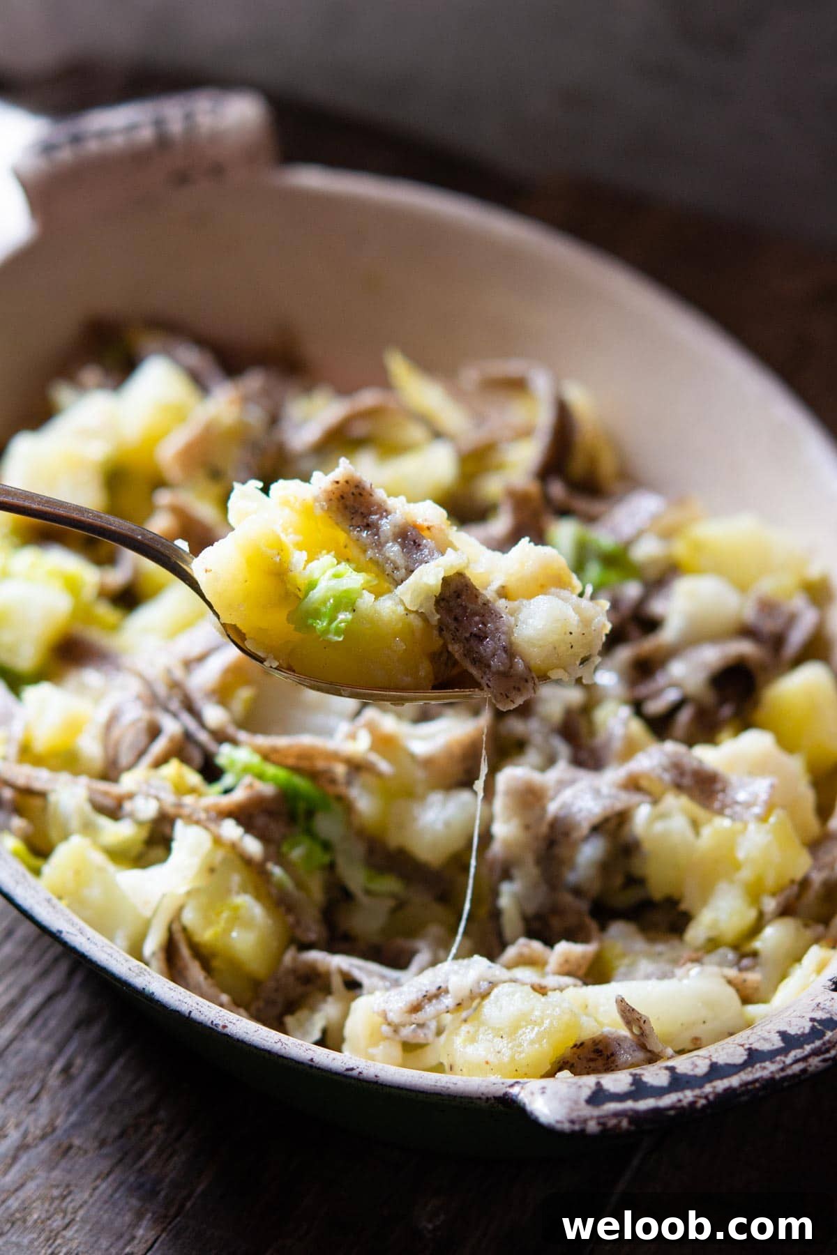 A close up of a spoonful of pizzoccheri pasta with potatoes, cabbage and cheese