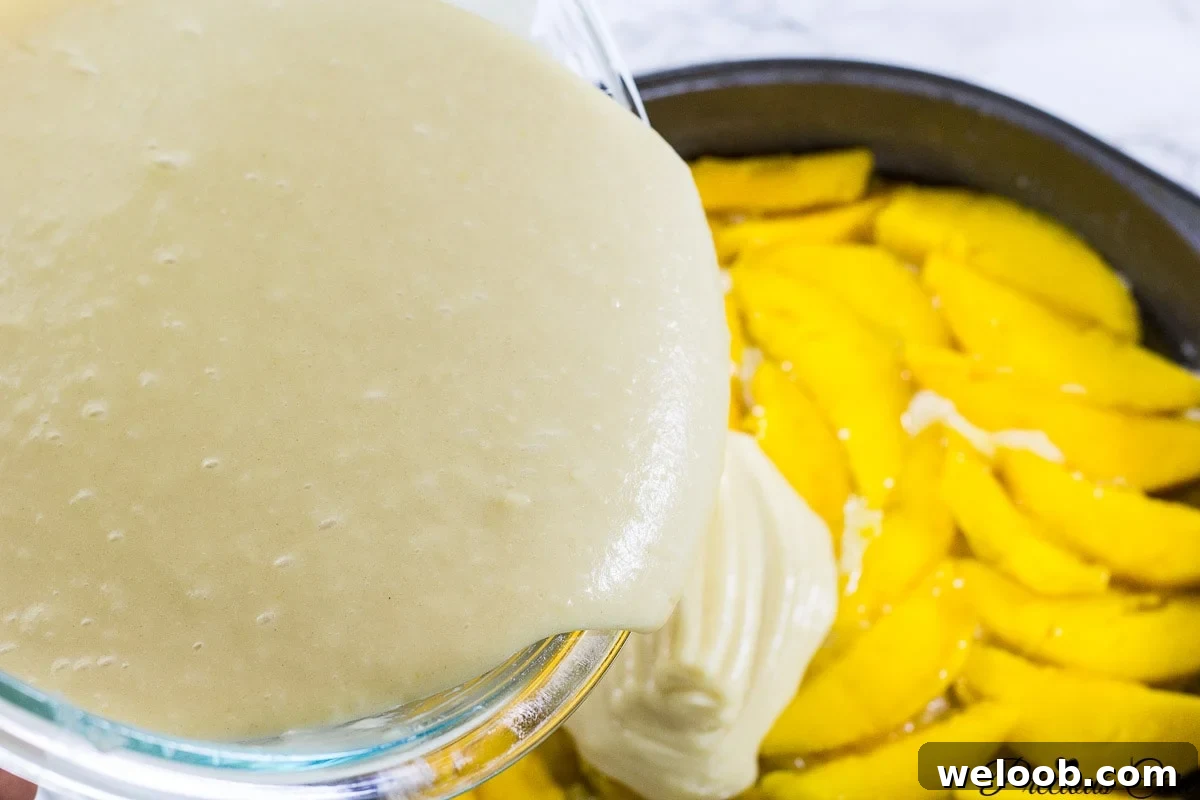 Cake batter pouring over sliced mangos.