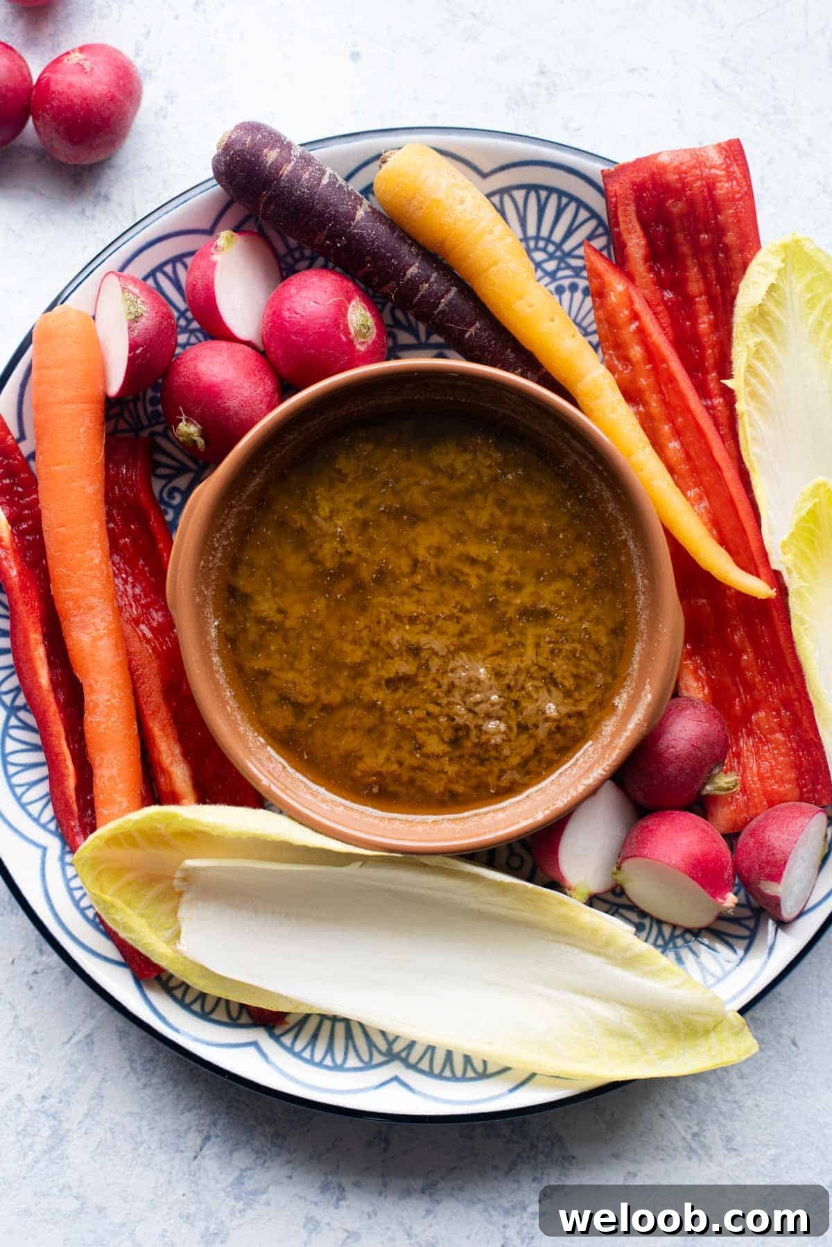 An overhead shot of Bagna Cauda in a terracotta dish with raw vegetables around it.