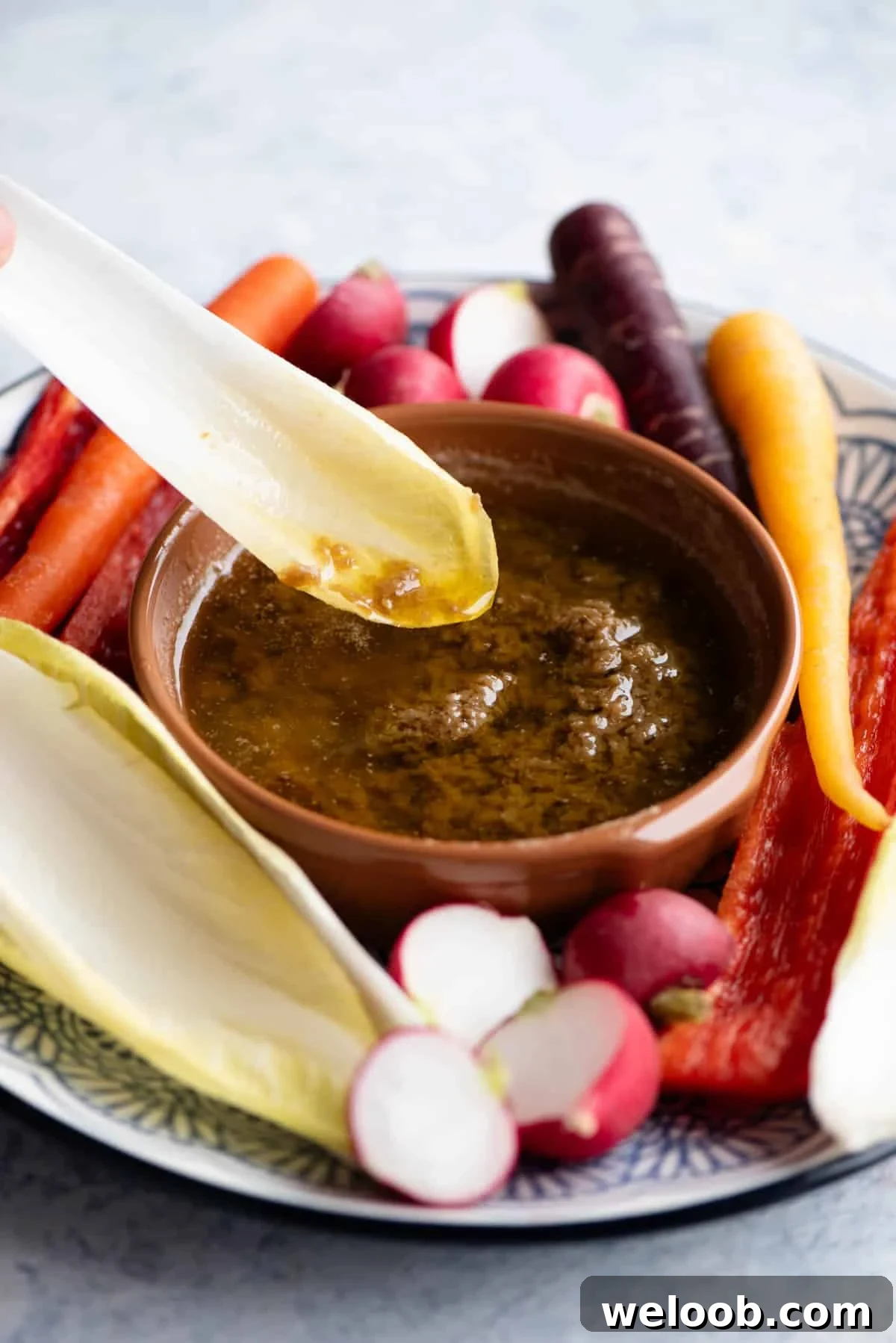 A close up of a piece of chicory being dunked into a Bagna Cauda dip.