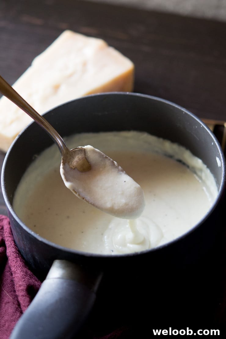 A close up shot of bechamel sauce in a saucepan with parmesan in background - how to make bechamel sauce recipe