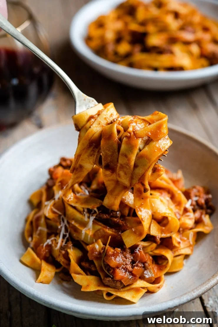 A fork picking up some beef ragu and pasta from a bowl.