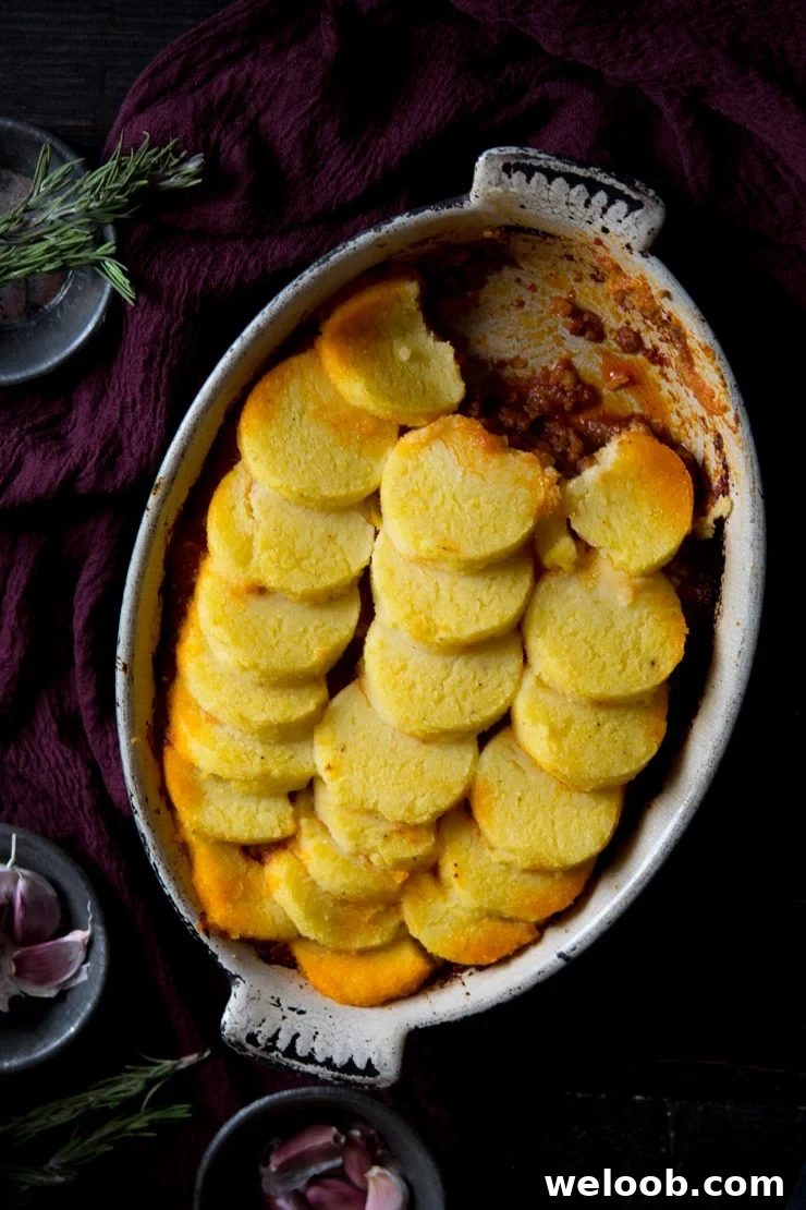 Beef and sausage ragu with baked polenta on top in an oval baking dish