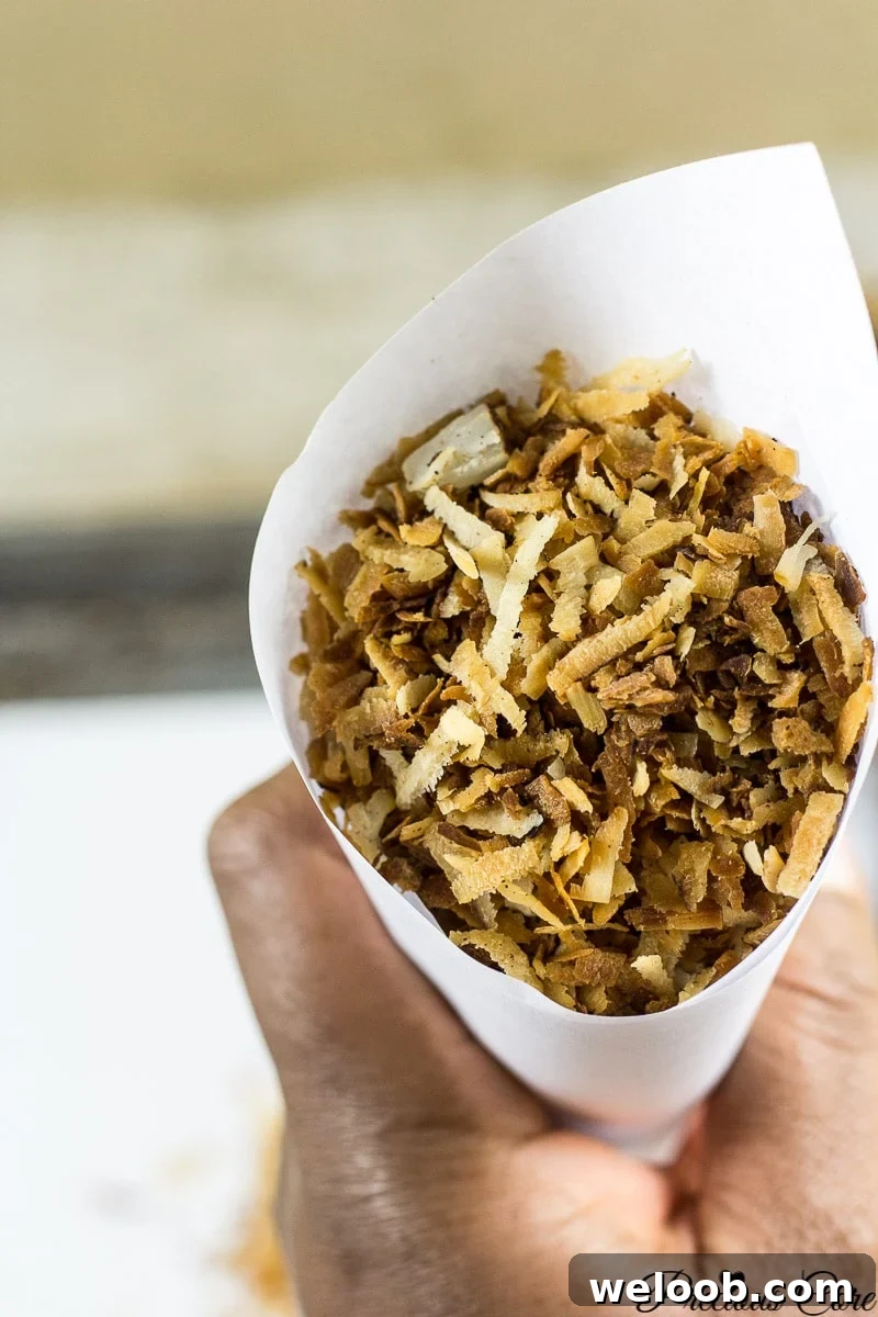 Person holding a paper cone of toasted coconut flakes.