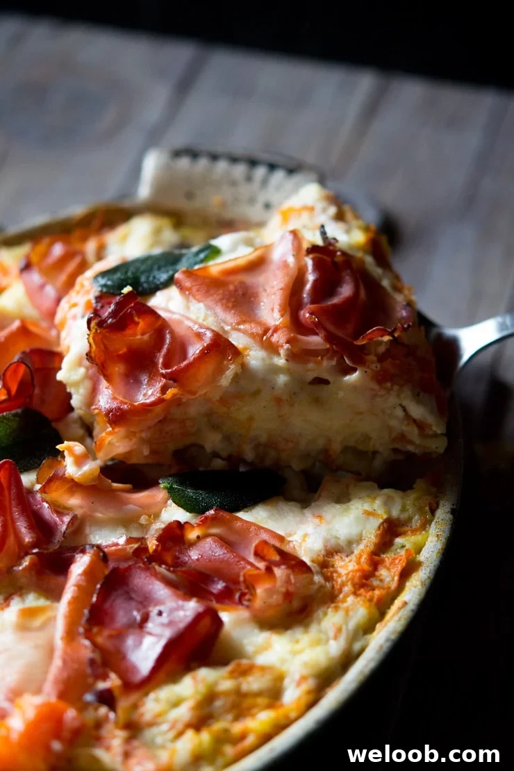A close up shot of a slice of butternut squash lasagna topped with prosciutto