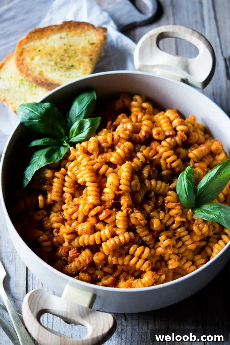 sun dried tomato pasta in a pot with basil and garlic bread