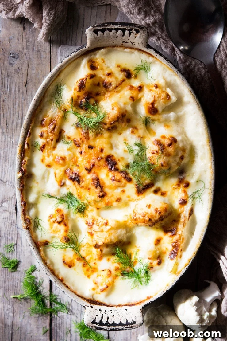 An overhead shot of baked cauliflower cheese in a oval baking dish on a wooden surface