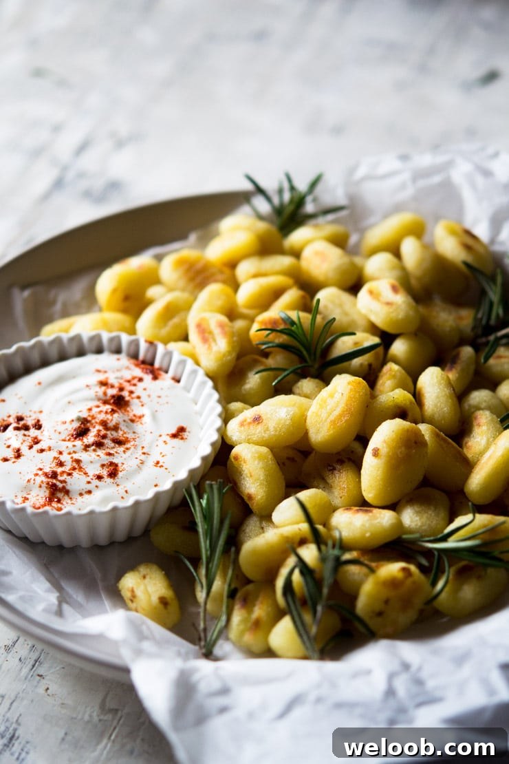 A close up of fried gnocchi on a plate with rosemary and a sour cream dip