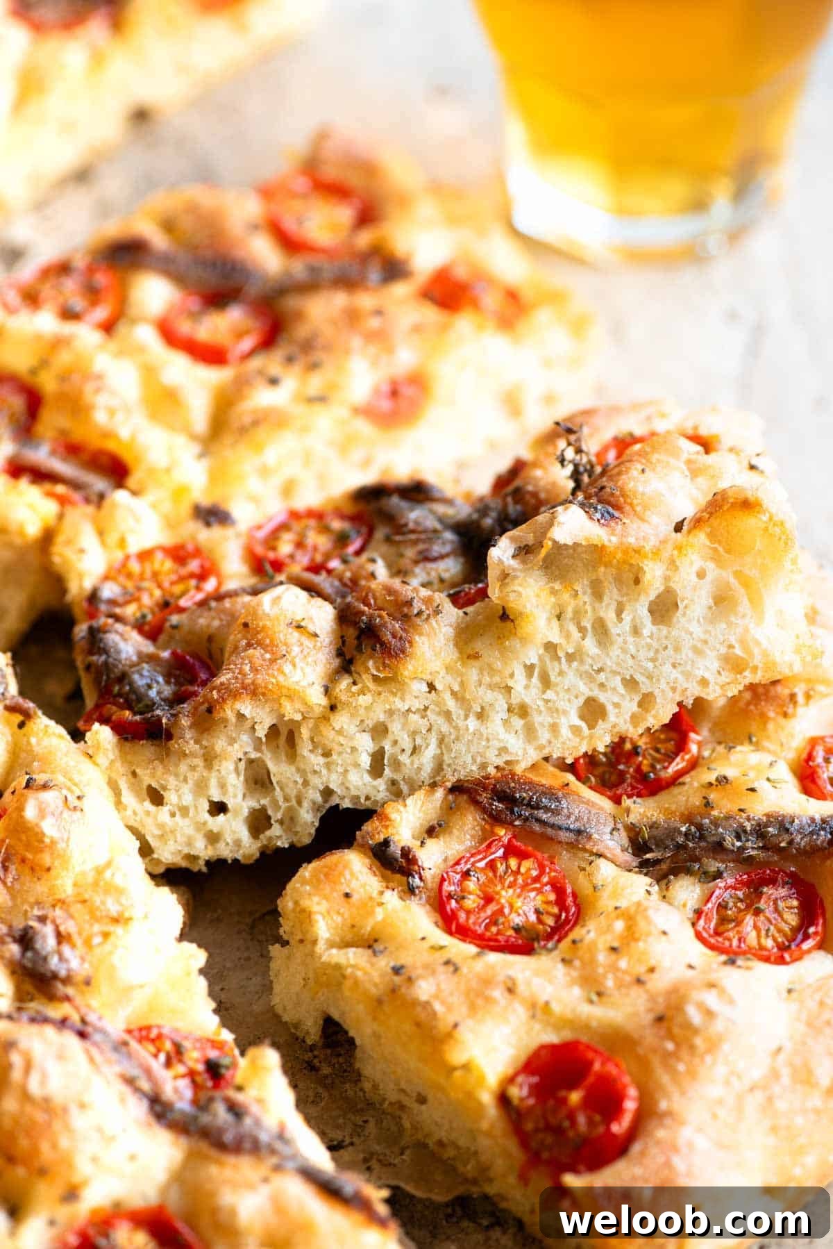 A close up of a slice of tomato and anchovy focaccia on it's side showing the airy and bubbly texture inside.